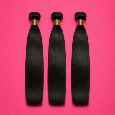 Three bundles of straight black hair extensions with gold ferrules on a bright pink background