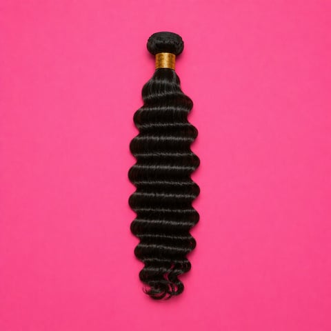 A single bundle of black wavy hair extension with a gold ferrule on a bright pink background